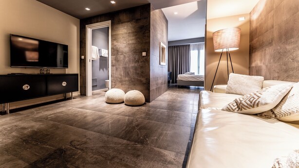 A modern bedroom with a large bed, a TV, a dark-toned wardrobe, and a floor lamp. - Neko Boutique Hotel (Cagliari)