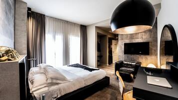 A modern hotel room with a bed, a desk, a chair, a TV, and a fireplace.