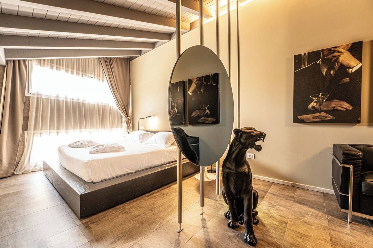 A modern hotel room with a bed, a desk, a chair, and a decorative sculpture.