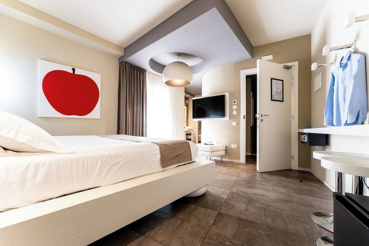 A modern hotel room with a large bed, a flat-screen TV, a dining area, and a bathroom.