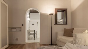 A modern bedroom with a bed, a floor lamp, a mirror, and a doorway leading to a bathroom. - Fori Imperiali Elegant Apartment (Rome)