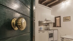 A compact kitchen with white cabinets, a stove, and a sink. - Fori Imperiali Elegant Apartment (Rome)