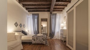 A bedroom with a wooden floor, a bed with a patterned bedspread, a sofa, and a bedside table with a lamp. - Fori Imperiali Elegant Apartment (Rome)