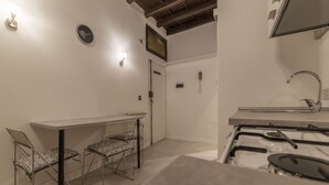 A compact kitchen with a gas stove, a sink, and a dining area with two chairs. - Fori Imperiali Elegant Apartment (Rome)