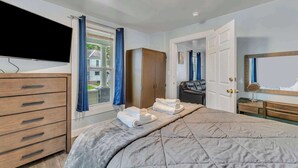 A bedroom with a bed, a wardrobe, a television, and a window with curtains. - Shortstop Apt 1 - All Star Baseball Rentals (Oneonta)