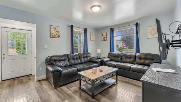 A living room with a sectional sofa, a coffee table, and a television. - Shortstop Apt 1 - All Star Baseball Rentals (Oneonta)