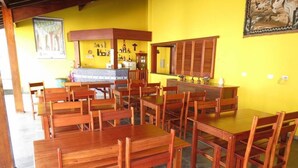 A dining area with wooden tables and chairs, a counter with bottles, and a yellow wall with a mural.