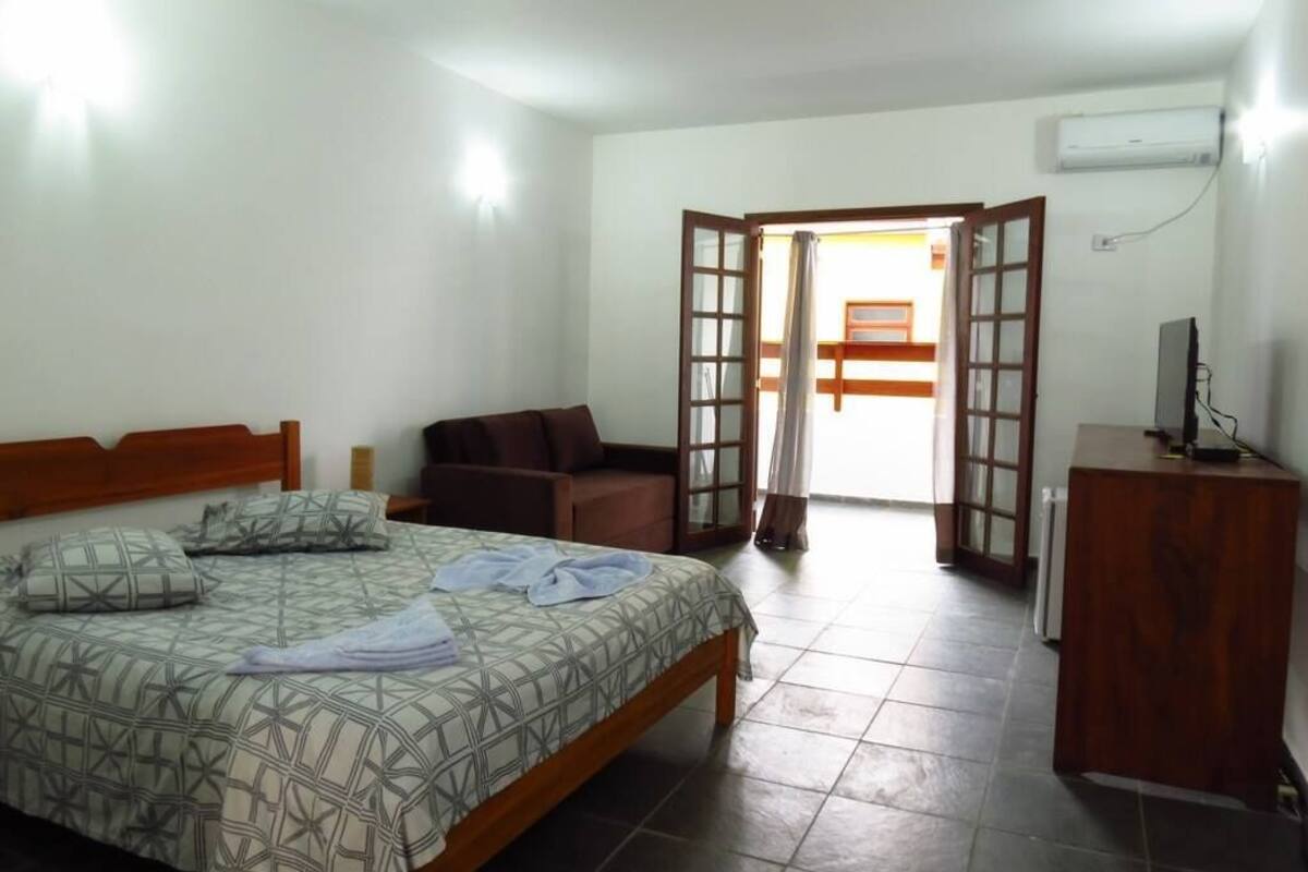 Quarto com cama, escrivaninha de madeira, cadeira e sofá.