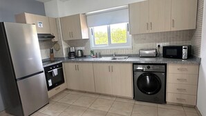 Una cocina moderna con un refrigerador de acero inoxidable, horno empotrado, microondas, cafetera y lavadora.
