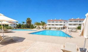A resort with two swimming pools, sun loungers, and a building with balconies. - Narcissos 'Nissi Beach' Apartment C12 (Ayia Napa)