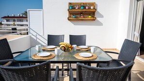 Una mesa de vidrio con cuatro sillas, un frutero y platos y tazas blancos.