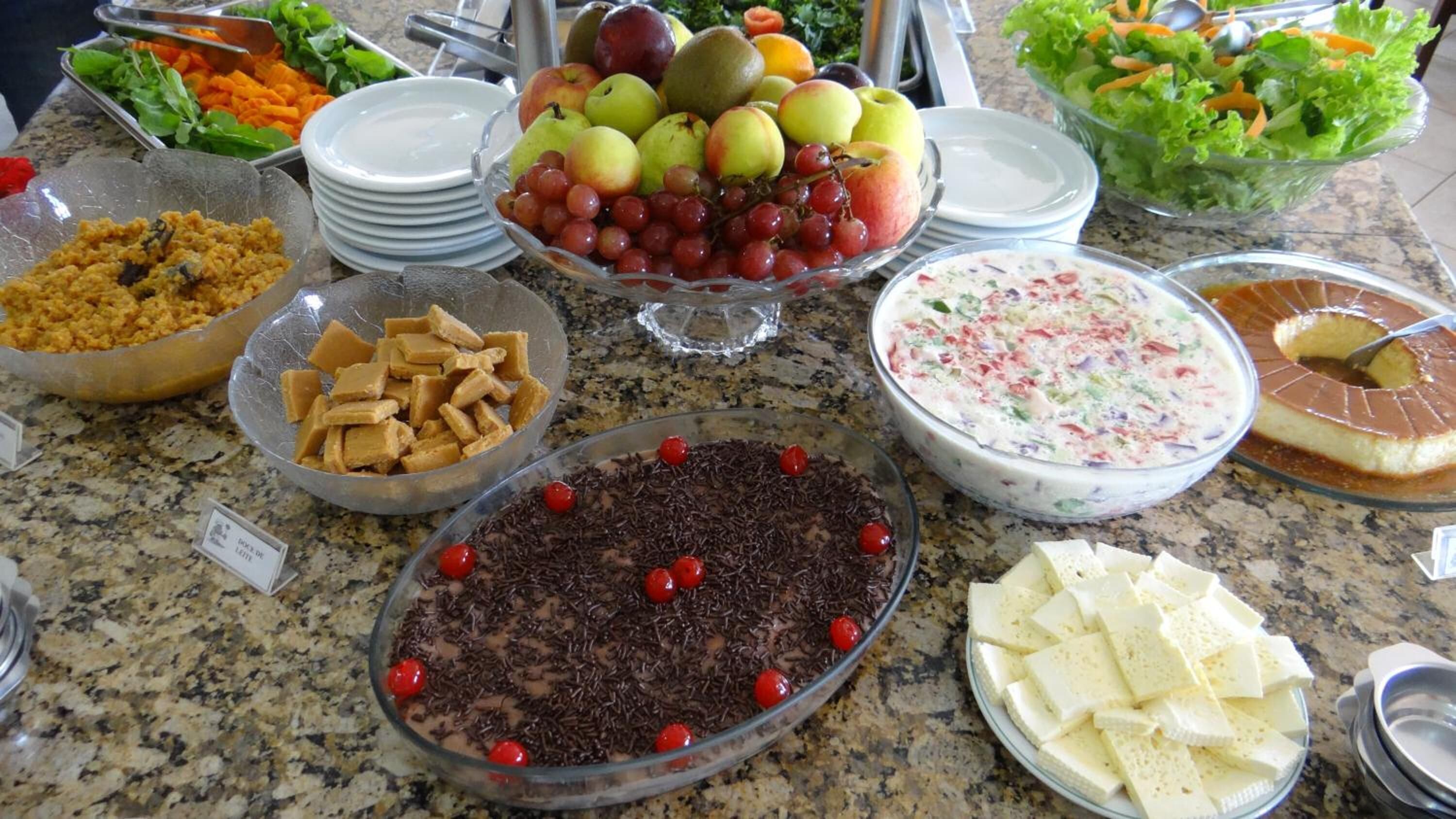 A buffet with various food items including fruits, a chocolate dessert, and a creamy salad.