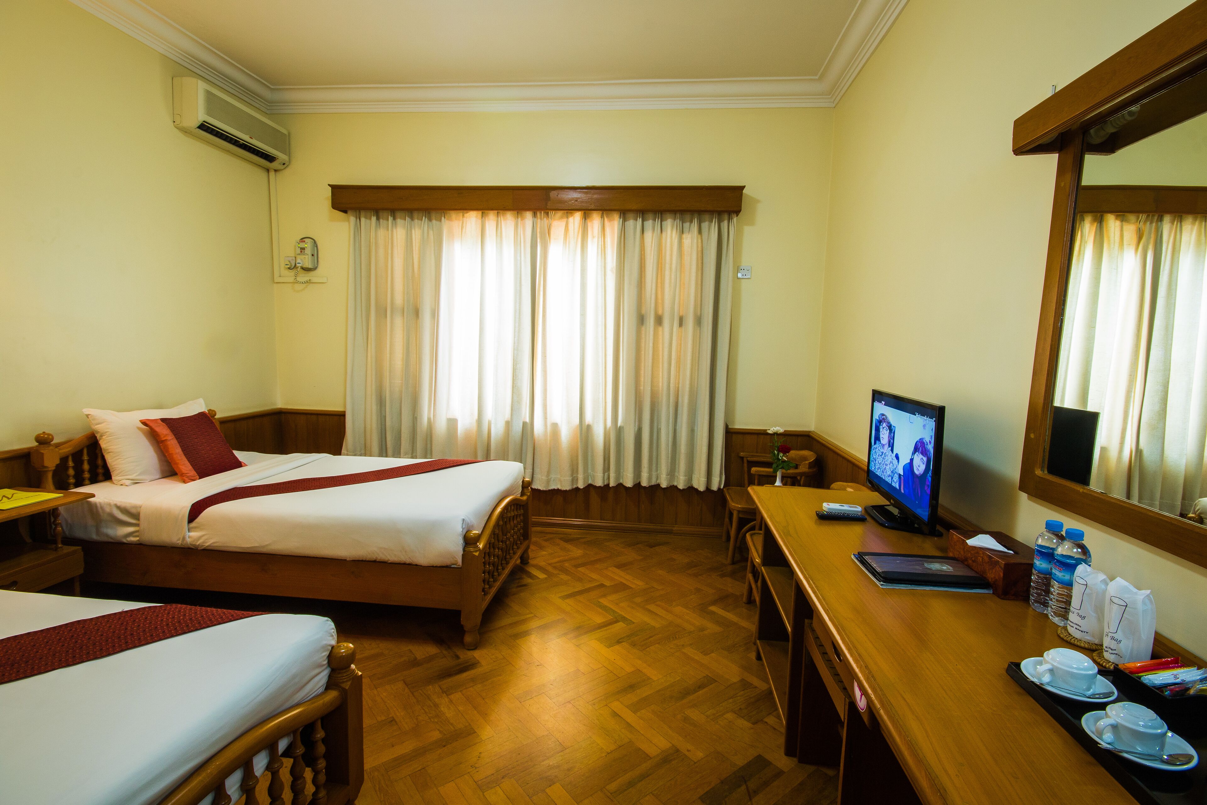 A hotel room with two beds, a desk with a computer, a TV, and a window with curtains.