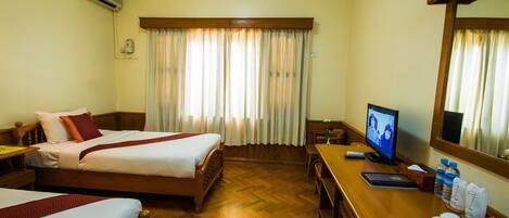 A hotel room with two beds, a desk with a computer, a TV, and a window with curtains.