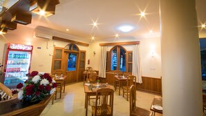 A hotel dining area with wooden furniture, a flower arrangement, and a refrigerator with beverages. - Win Unity Pyin Oo Lwin (Pyin Oo Lwin)