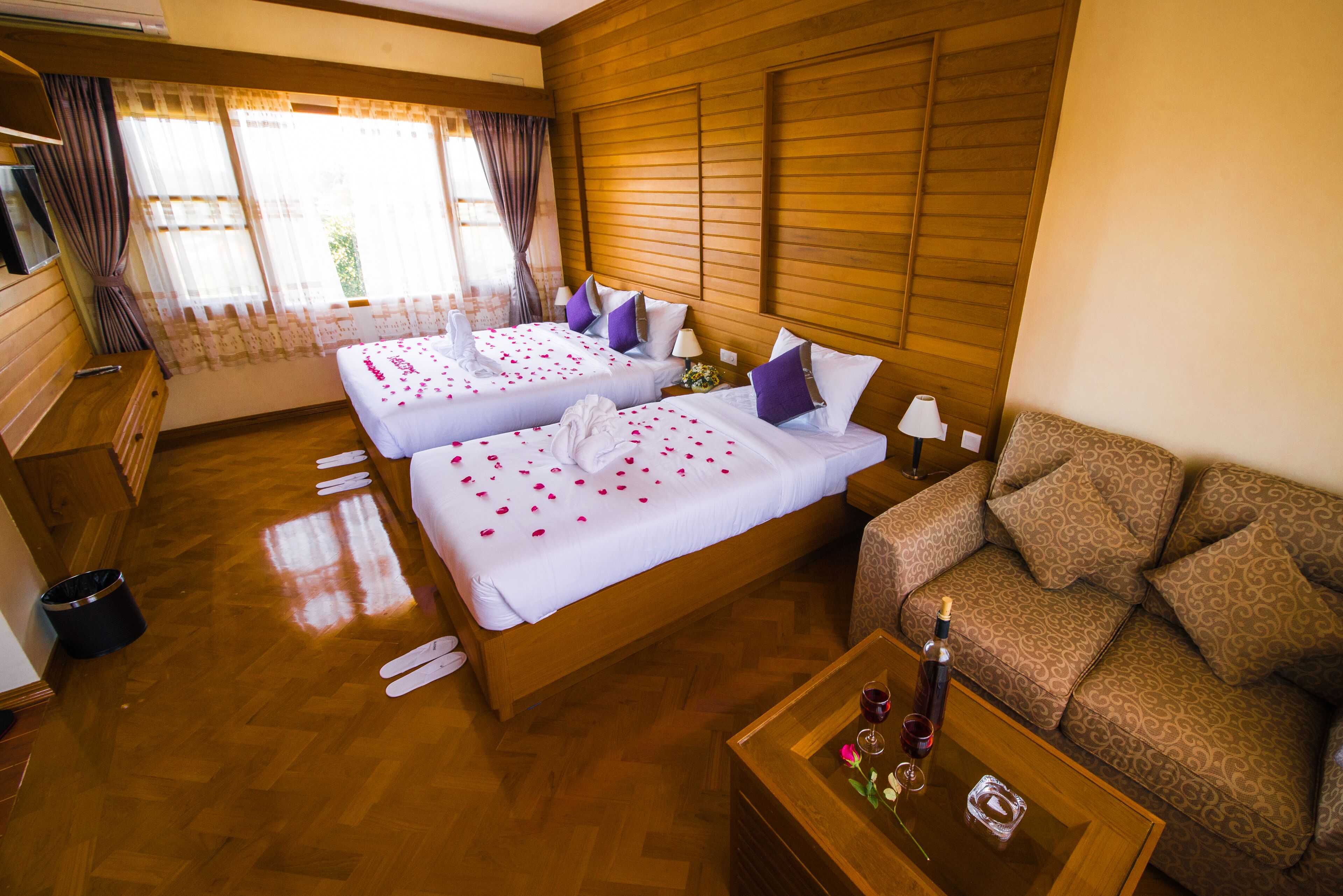 A hotel room with two beds, a sofa, a wooden floor, and a window with curtains.