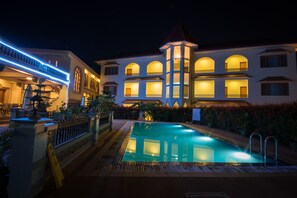 A hotel with a swimming pool, a covered outdoor area, and a well-lit facade at night.