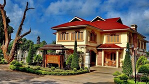 A two-story hotel with a red roof and beige walls, featuring a large entrance and a signboard. - Win Unity Pyin Oo Lwin (Pyin Oo Lwin)