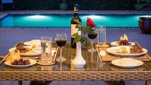 A dining table with plates of food, glasses of wine, and a bottle of wine, set outdoors with a pool in the background. - Win Unity Pyin Oo Lwin (Pyin Oo Lwin)