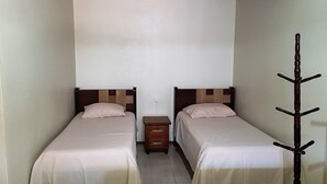 A small, narrow room with two single beds, a wooden nightstand between them, and a coat rack to the right. - Hotel Dal Cortivo (Candiota)