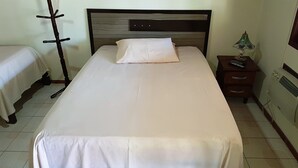 A neatly made bed with a white sheet and pillow, a wooden nightstand with a lamp, and a radiator on the wall. - Hotel Dal Cortivo (Candiota)