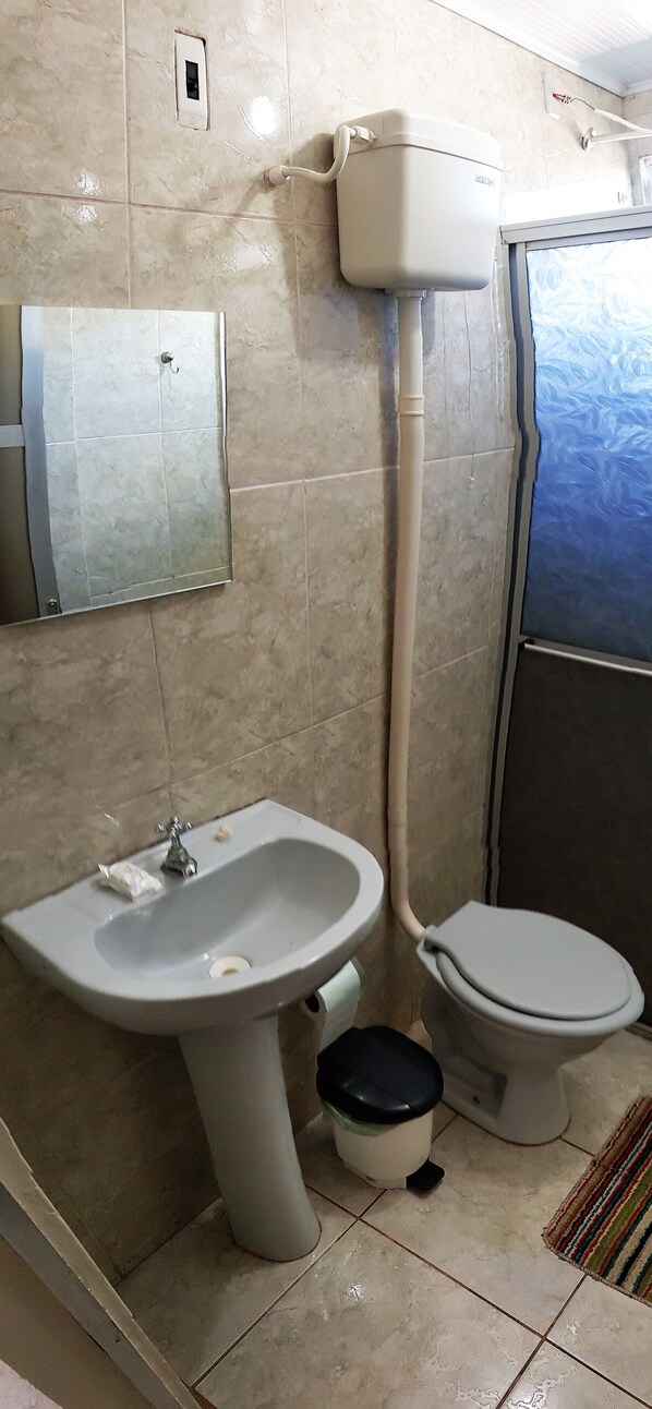 Un baño con lavamanos, inodoro y una tubería a la vista.
