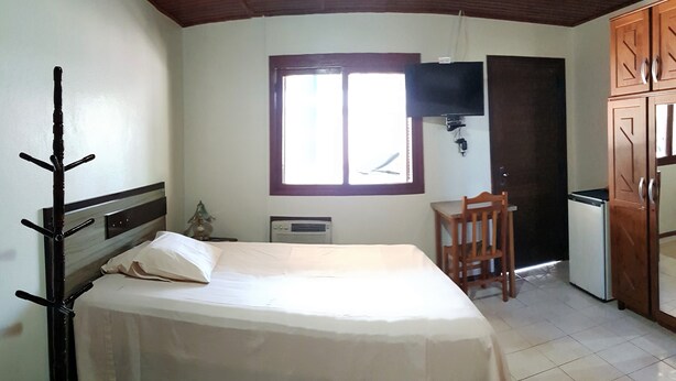 A bedroom with a bed, a wooden chair, a desk, a window, and a wardrobe. - Hotel Dal Cortivo (Candiota)