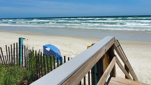 Una passerella in legno che conduce a una spiaggia con un ombrellone blu e una recinzione.
