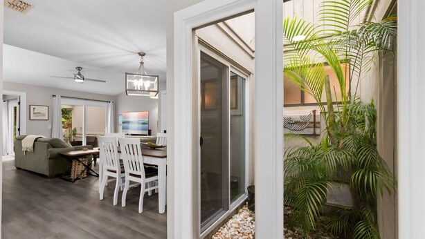 Un soggiorno moderno con zona pranzo, una ventola a soffitto e vista su un giardino tramite una porta scorrevole in vetro.