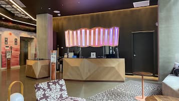 A hotel reception area with a modern design, including a reception desk, seating area, and elevator.
