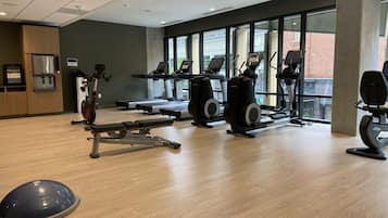 A gym with cardio machines, weight equipment, and a large window offering a view of the outside.