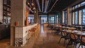 Un interior de restaurante moderno con una zona de bar, techos altos y ventanas amplias.