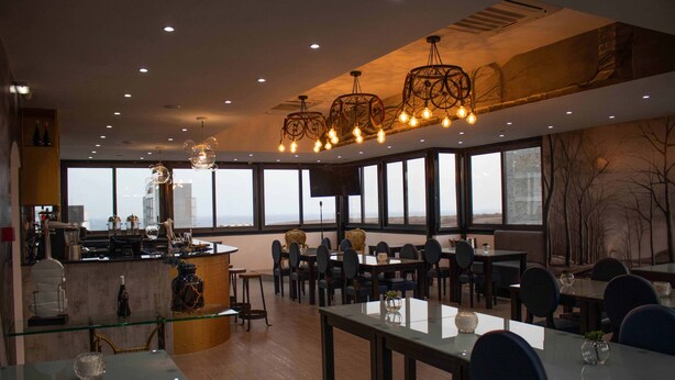 Un restaurante moderno con una zona de bar, grandes ventanales e iluminación contemporánea.
