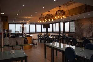 Een modern restaurant met een bar, grote ramen en moderne verlichtingsarmaturen.