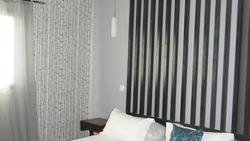 A modern bedroom with a bed, white bedding, a teal-patterned throw, and a vertical black and white striped wall.