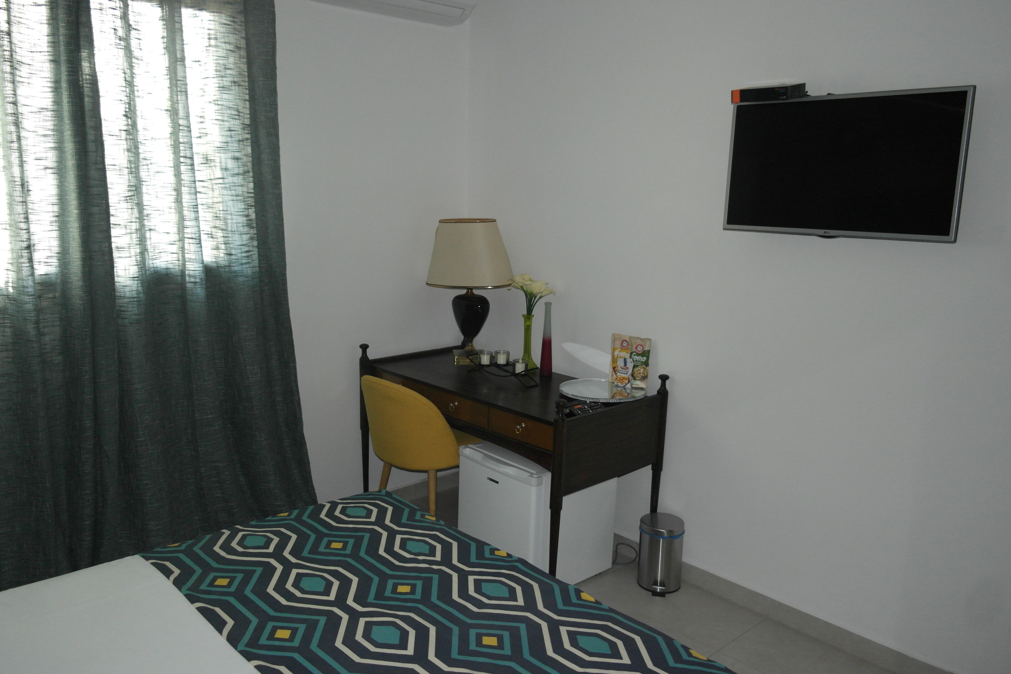 A small hotel room with a bed, a desk with a chair, a TV, a lamp, and a trash bin.