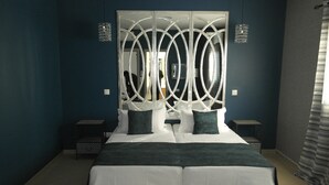 Cama doble con colcha blanca y azul verdosa, dos mesitas de noche y un cabecero decorativo con diseños circulares.