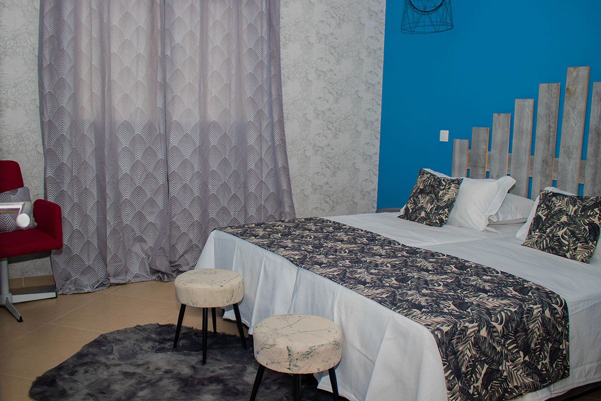 Un dormitorio con una cama, dos taburetes, una silla roja y una cortina estampada.