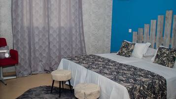 Un dormitorio con una cama, dos taburetes, una silla roja y una cortina estampada.