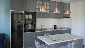 Cocina moderna con gabinetes grises, un refrigerador de acero inoxidable, encimera de mármol e iluminación colgante.
