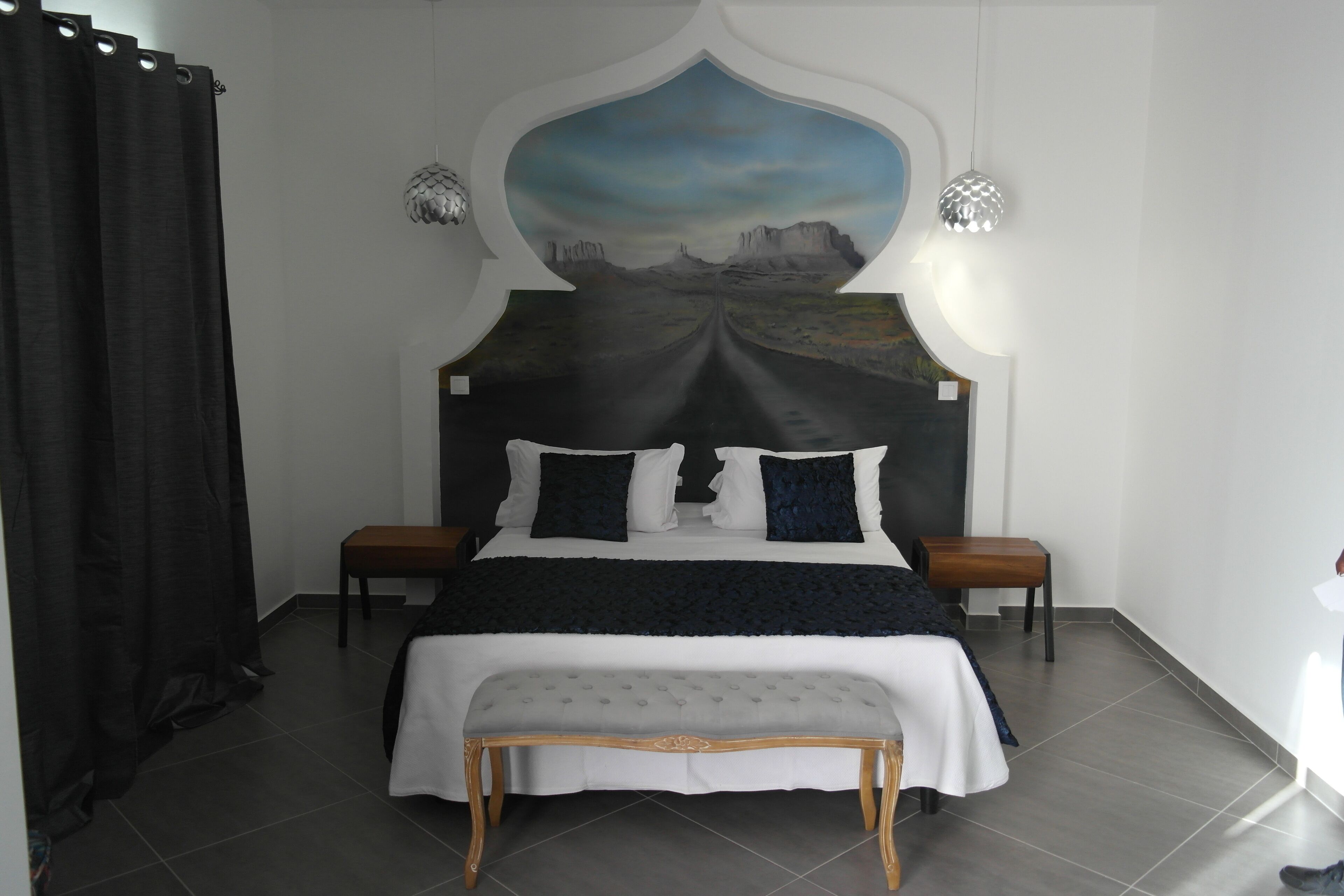 A bedroom with a large bed, a bench, two nightstands, and a wall mural.