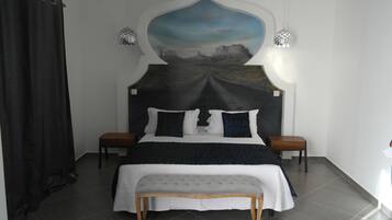 Un dormitorio con una cama grande, un banco, dos mesitas de noche y un mural en la pared.