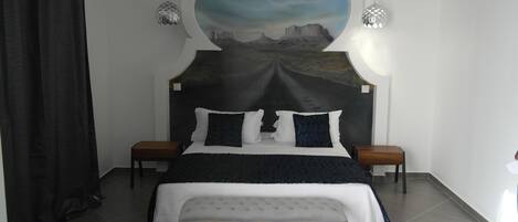Un dormitorio con una cama grande, un banco, dos mesitas de noche y un mural en la pared.