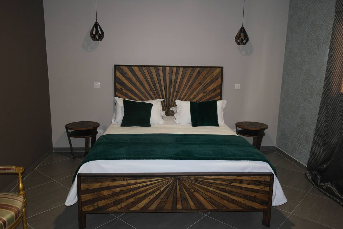 A neatly made bed with a wooden headboard, two bedside tables, and a green throw blanket.