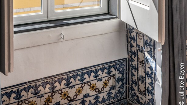 A room with a window revealing a yellow building with multiple windows. - Azulejos Cais Sodré B&B (Lisbon)
