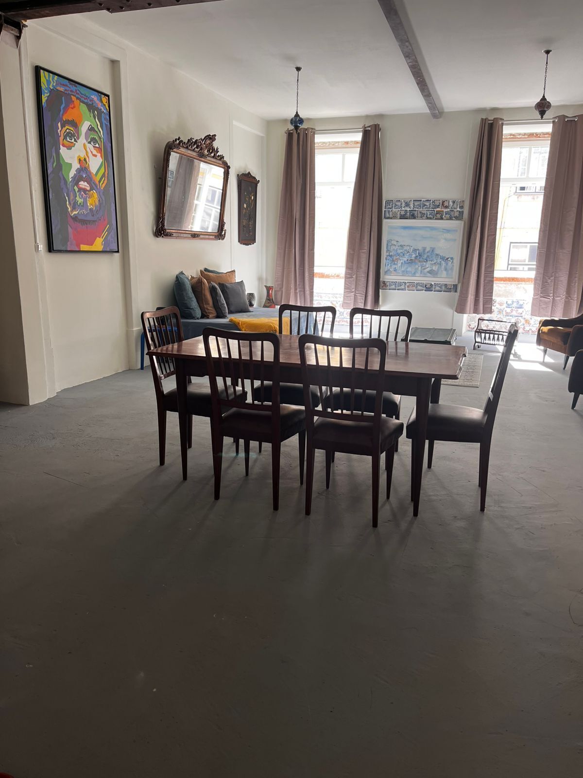 A dining area with a wooden table and chairs, a sofa with cushions, and a large painting on the wall.