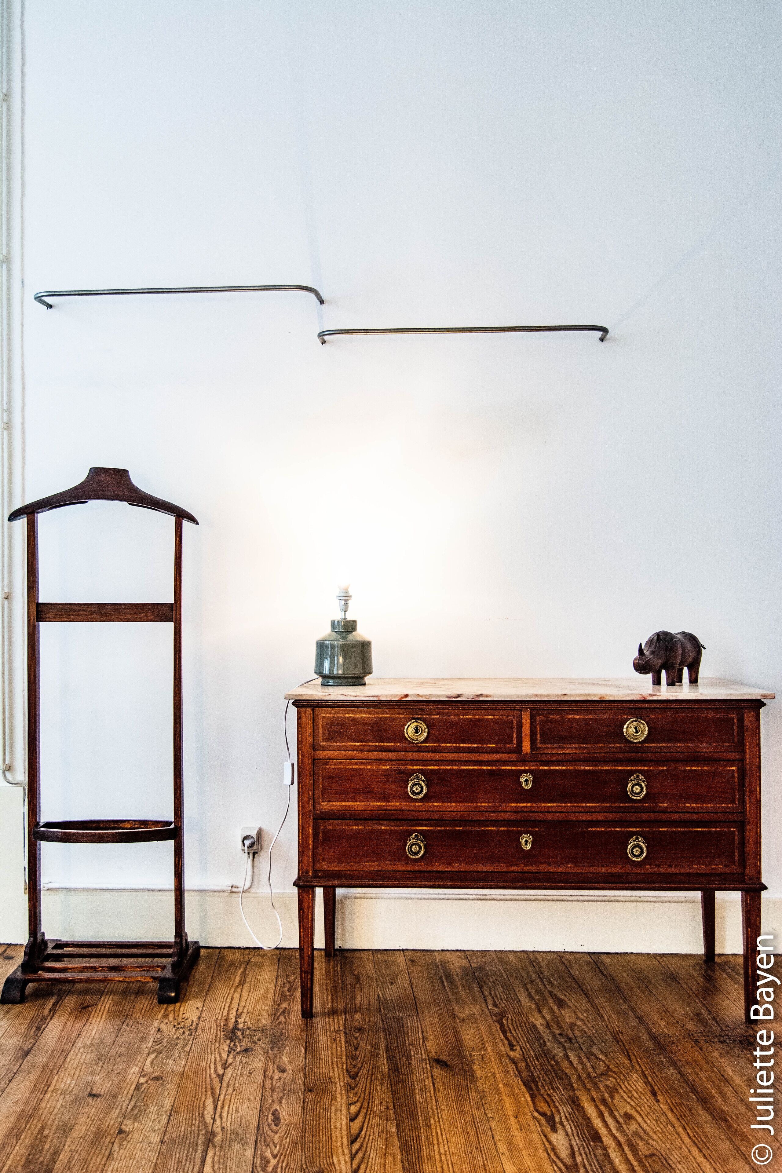 A wooden dresser with drawers and a small figurine, a wooden coat rack, and a marble countertop with a lamp.
