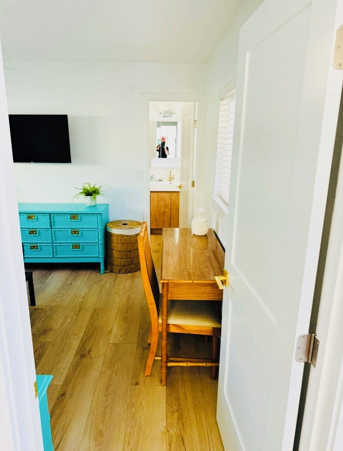 A narrow hallway with a wooden floor, a teal dresser with drawers, a small round table, and a chair.