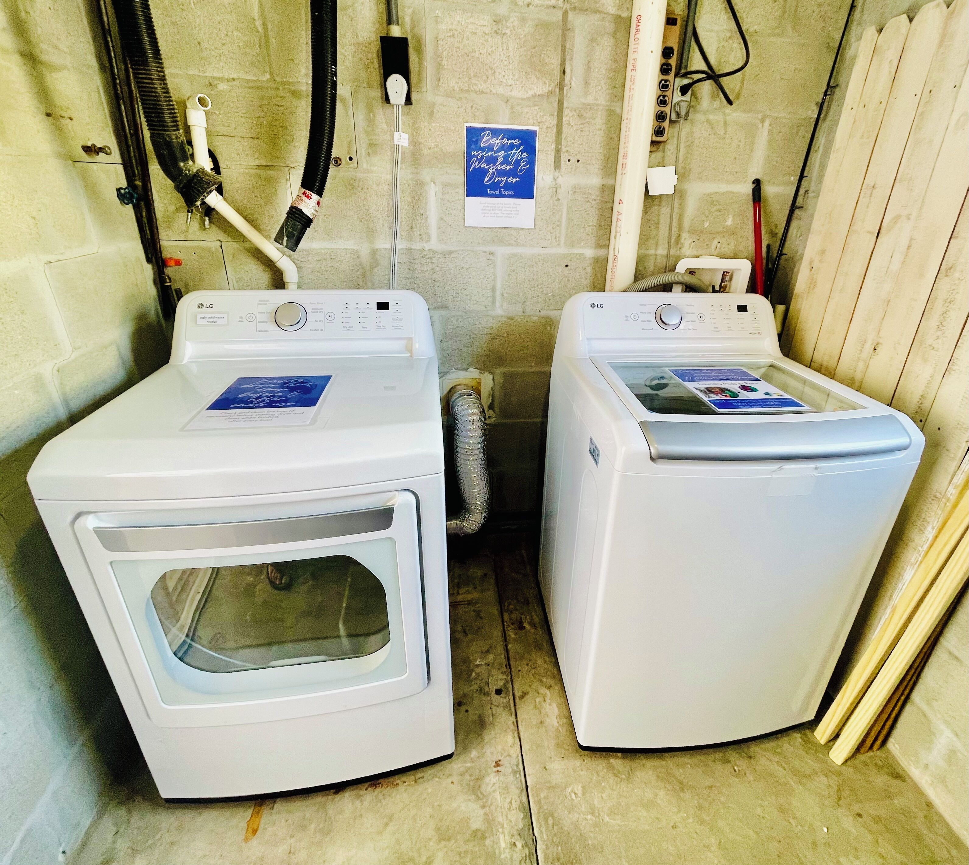 Two white front-loading washers with control panels, a blue sign on the wall, and a wooden door in a laundry room.