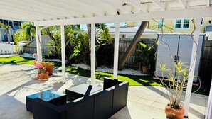 An outdoor patio area with a black wicker sofa, a glass-top table, and potted plants. - Steps to the Beach, No Car Needed, Completely Permitted Remodel + King Size Bed! (Indian Rocks Beach)